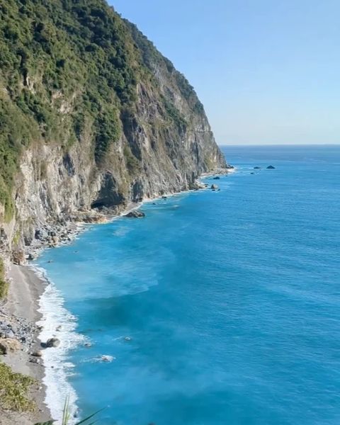 A green cliffside coastline dropping into a bright blue sea