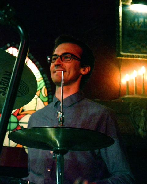 Adam playing drums on stage, smiling, behind a cymbal