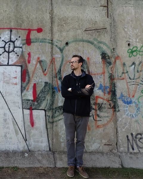 Adam standing with arms crossed in front of a graffiti-covered concrete wall
