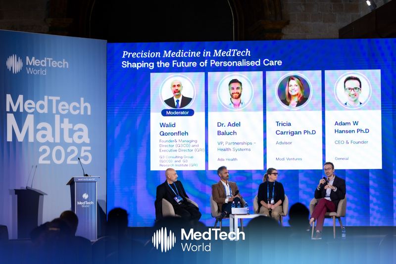 Adam Hansen speaking on a four-person precision medicine panel at MedTech Malta 2025, in front of a screen showing the panel title and panelists