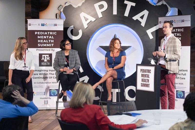 Adam Hansen at the podium moderating a three-person panel at the Pediatric Mental Health Summit in Austin